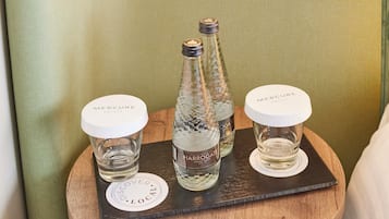 A wooden tray with two bottles of water and two glasses on a round wooden table against a green wall.