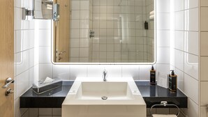 A modern bathroom with a large mirror, a white sink, a black countertop, and a towel rack.