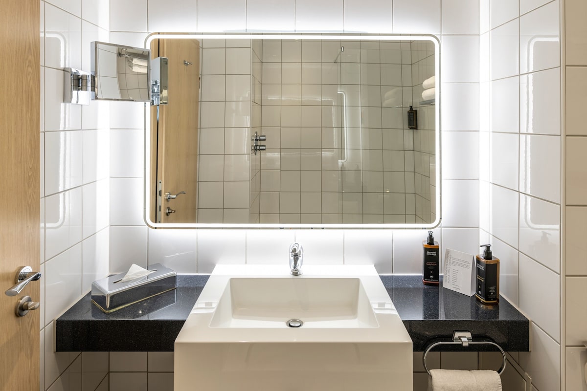A modern bathroom with a large mirror, a white sink, a black countertop, and a towel rack.