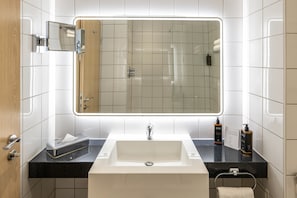 A modern bathroom with a large mirror, a white sink, a black countertop, and a towel rack.