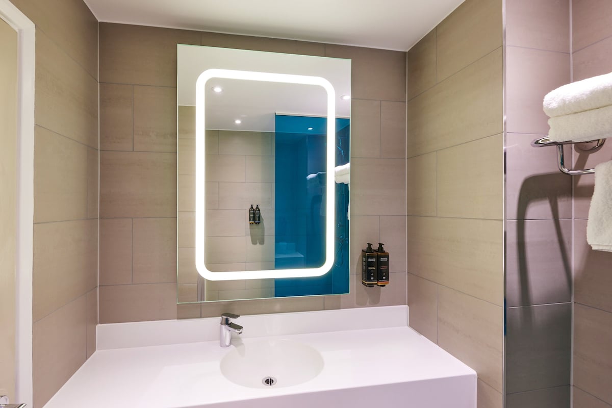 A bathroom with a white sink, a mirror with illuminated edges, and a towel rack.