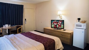 Une chambre d’hôtel comprenant un lit, un bureau avec une chaise, une télévision, un four à micro-ondes et une lampe.