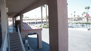 A covered outdoor area with a pool, palm trees, and a building with a red-tiled roof in the background. - Red Roof Inn Blythe (Blythe)