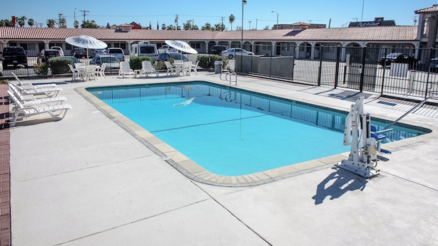 A rectangular swimming pool with a tiled deck surrounding it, equipped with lounge chairs and umbrellas. - Red Roof Inn Blythe (Blythe)