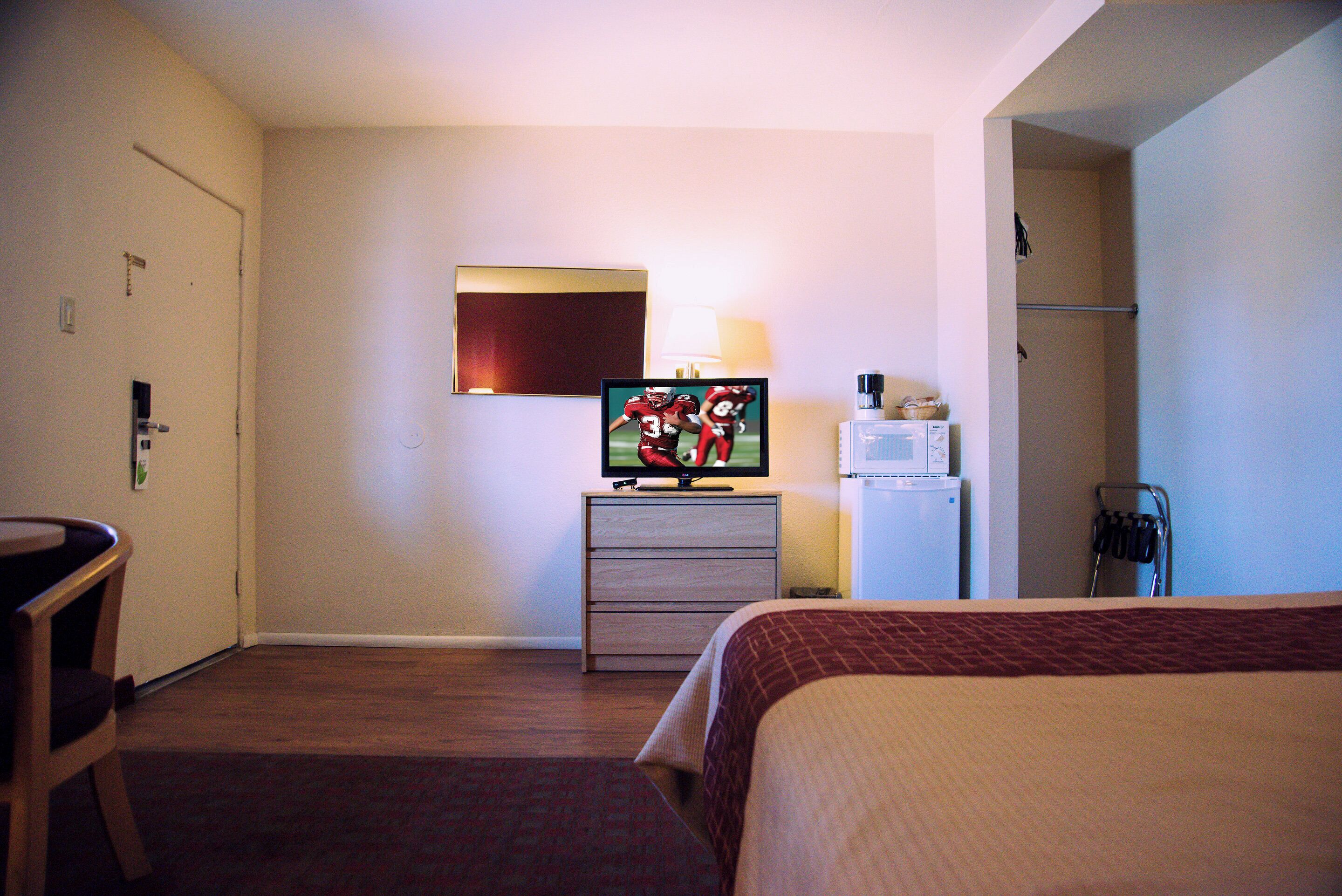 A hotel room with a bed, a desk, a television, a refrigerator, and a microwave.