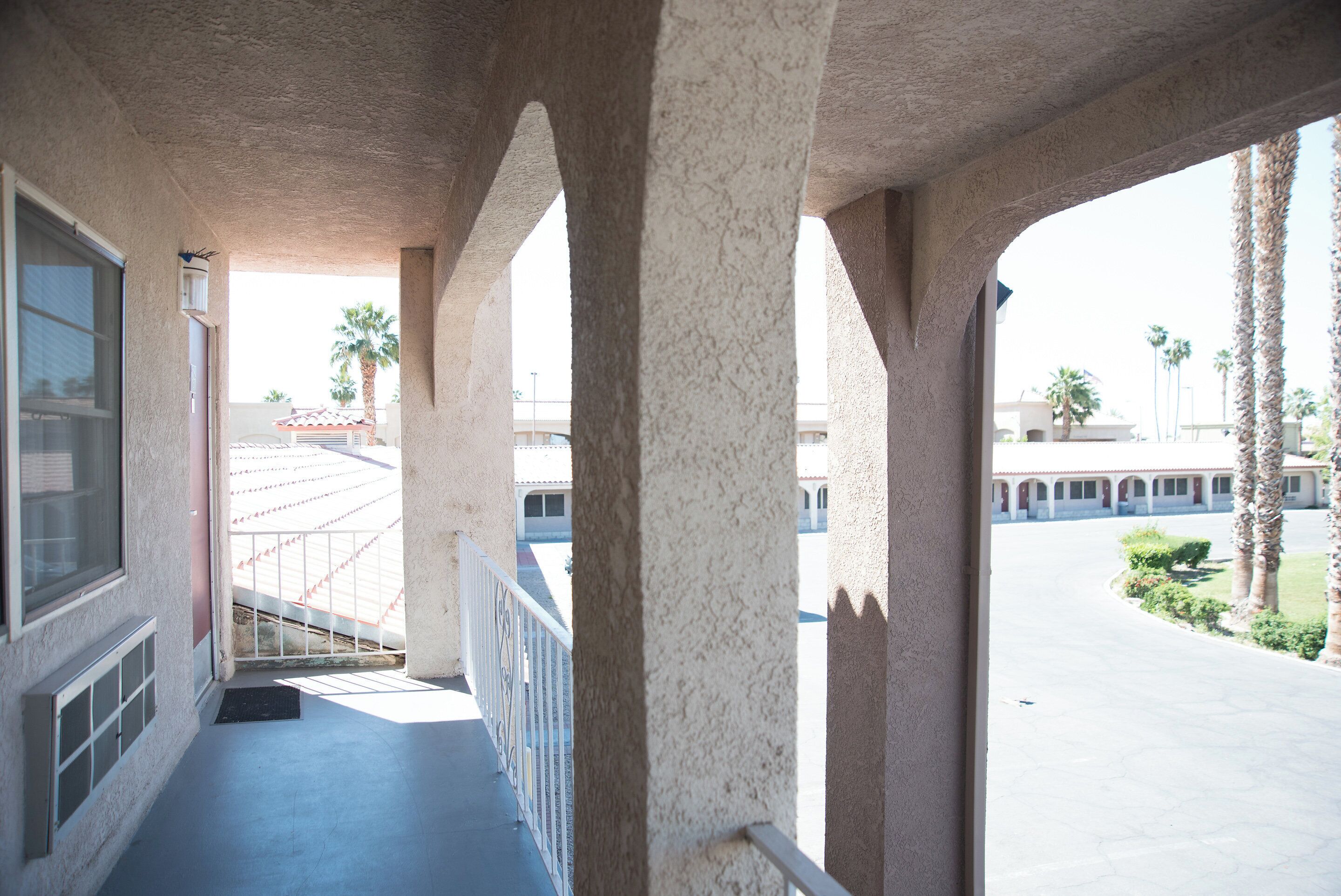 A covered balcony with a view of a parking lot and palm trees.