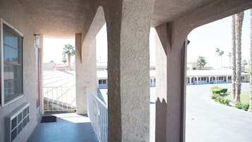 A covered balcony with a view of a parking lot and palm trees.