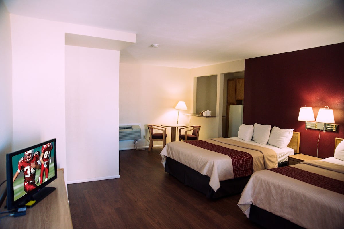 A hotel room with two beds, a TV, a desk with a chair, and a lamp.