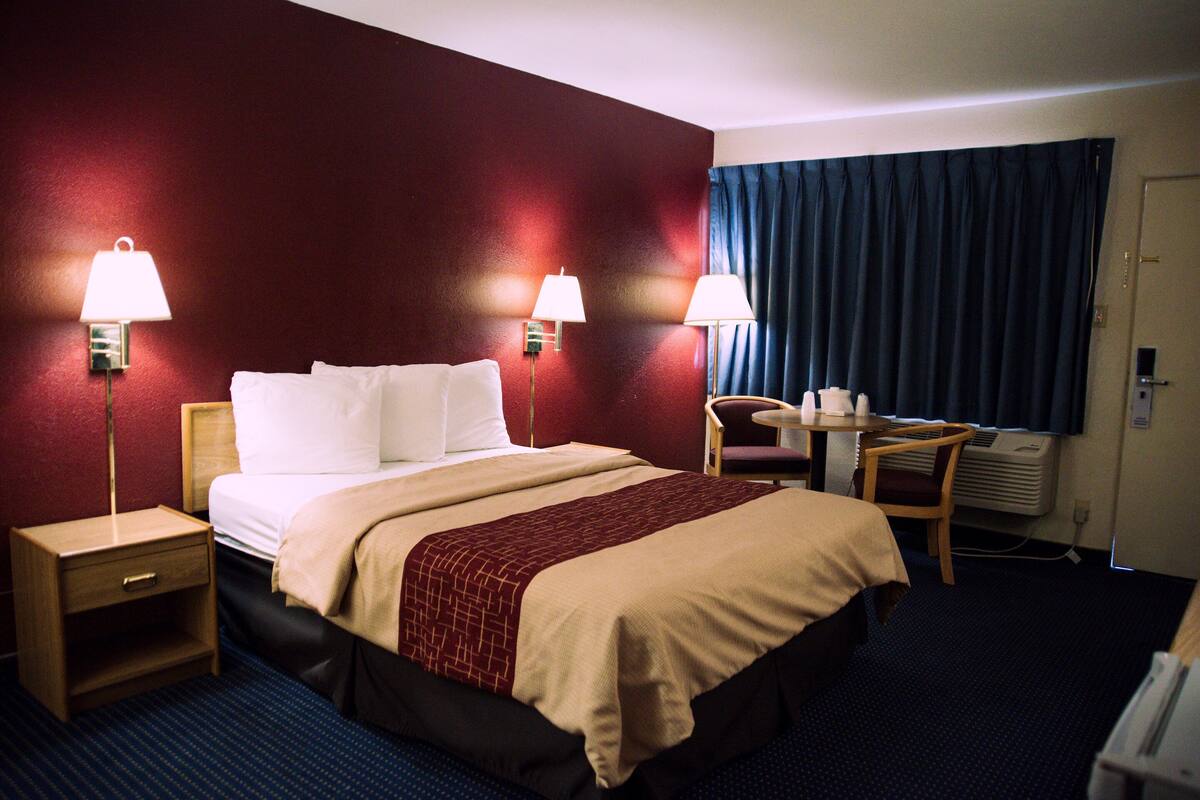 Ein Hotelzimmer mit einem Bett, zwei Nachttischlampen, einem Schreibtisch mit Stuhl und einem Fenster mit Vorhängen.