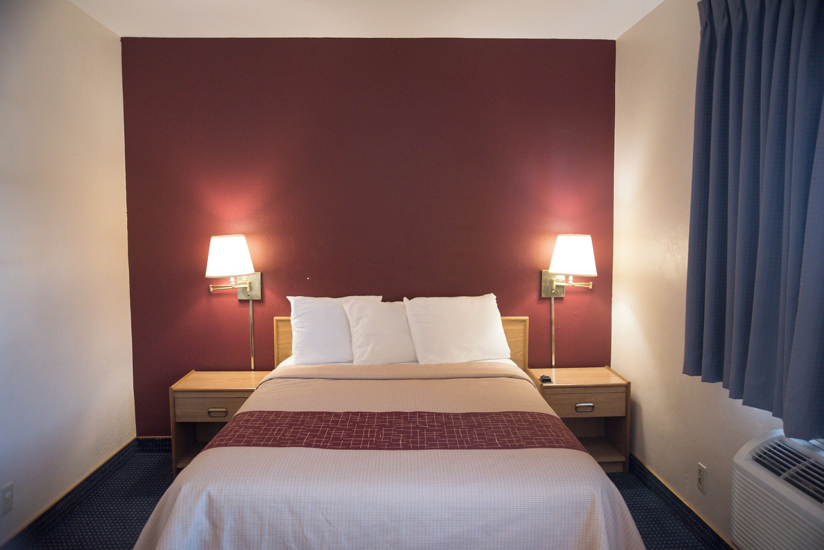 Une chambre d’hôtel avec un grand lit, deux lampes de chevet, un radiateur et une fenêtre avec des rideaux.