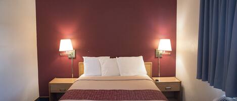 Une chambre d’hôtel avec un grand lit, deux lampes de chevet, un radiateur et une fenêtre avec des rideaux.
