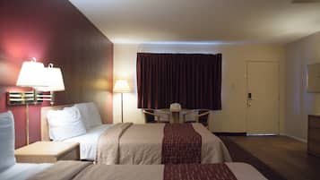 A hotel room with two beds, a desk, a chair, a lamp, a door, and a window with curtains.