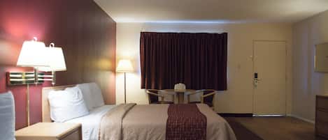Une chambre d’hôtel avec deux lits, un bureau, une chaise, une lampe, une porte et une fenêtre avec des rideaux.