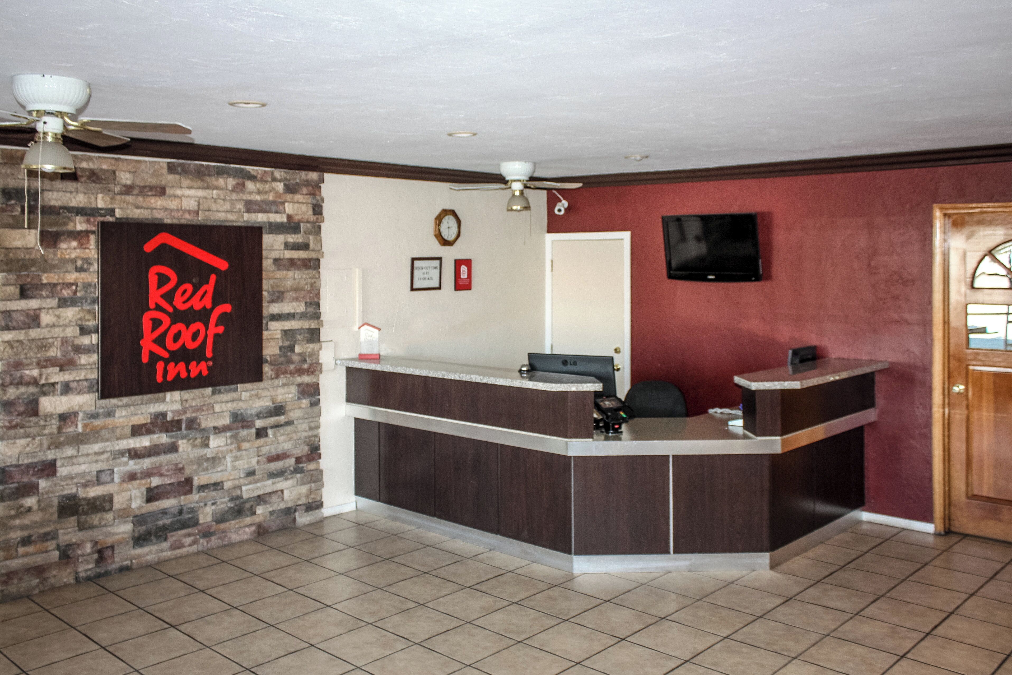 Una zona de recepción con el letrero de Red Roof Inn, un reloj, un televisor de pantalla plana y un mostrador de recepción.
