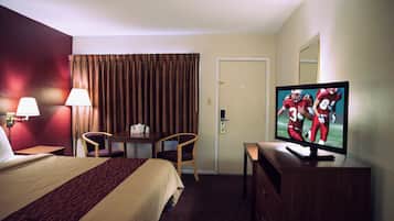 A hotel room with a bed, a desk, a television, and a door.