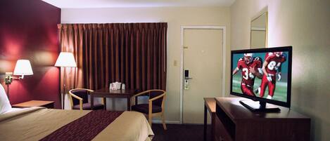 Una habitación de hotel con cama, escritorio, televisor y puerta.