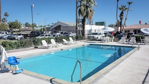 A swimming pool with lounge chairs and umbrellas, surrounded by a fence and palm trees. - Red Roof Inn Blythe (Blythe)