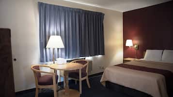Een hotelkamer met een bed, een bureau met twee stoelen, een raam met gordijnen en een wandlamp.