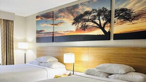Habitació d'hotel amb dos llits, un quadre gran d'un capvespre i una làmpada sobre una taula de nit.