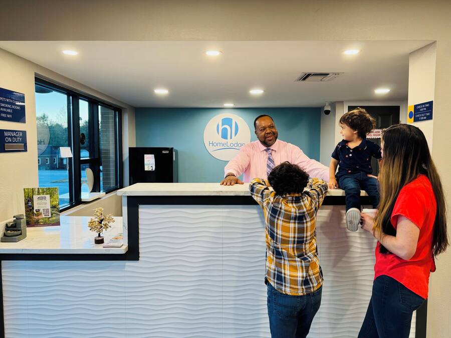A reception desk with a logo, a refrigerator, and a window with a view of the outside.
