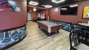 Una sala de billar con mesa de pool, sillas y el logotipo de Bud Light en la pared.