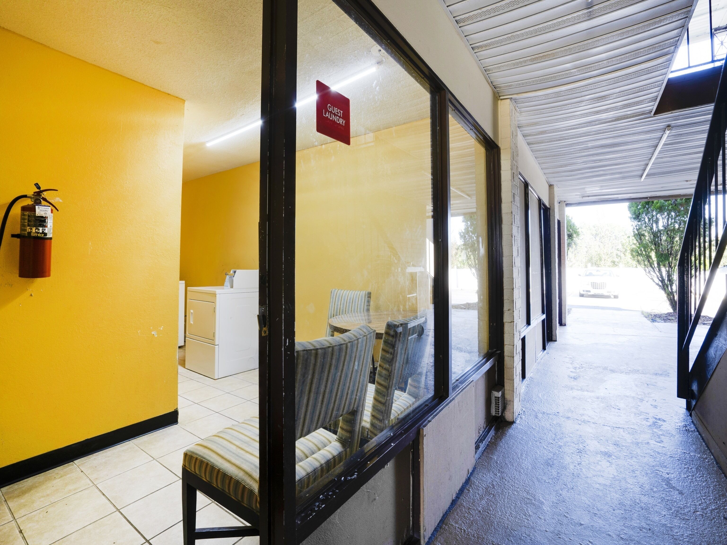 A hallway with yellow walls, a fire extinguisher, a sign for guest laundry, and a row of chairs.