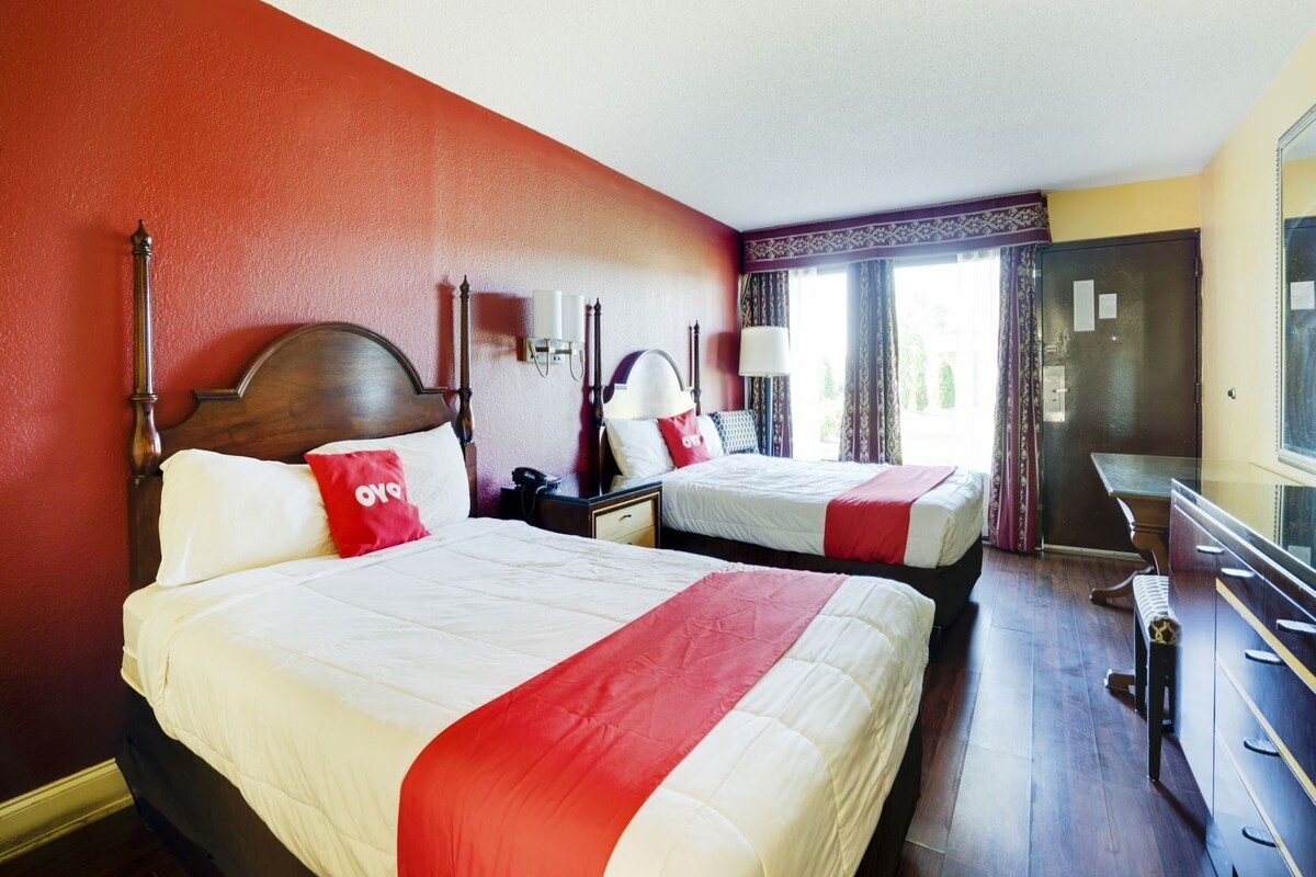 A hotel room with two beds, a desk, and a mirror.