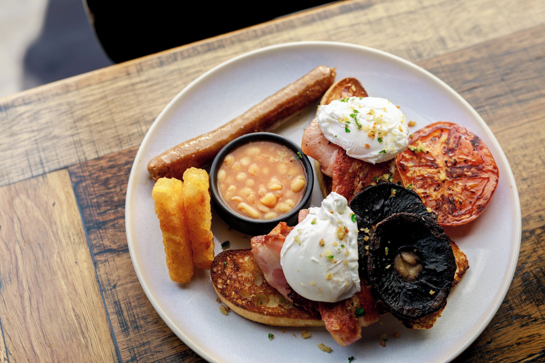 A plate with bacon, eggs, toast, beans, and a grilled tomato.