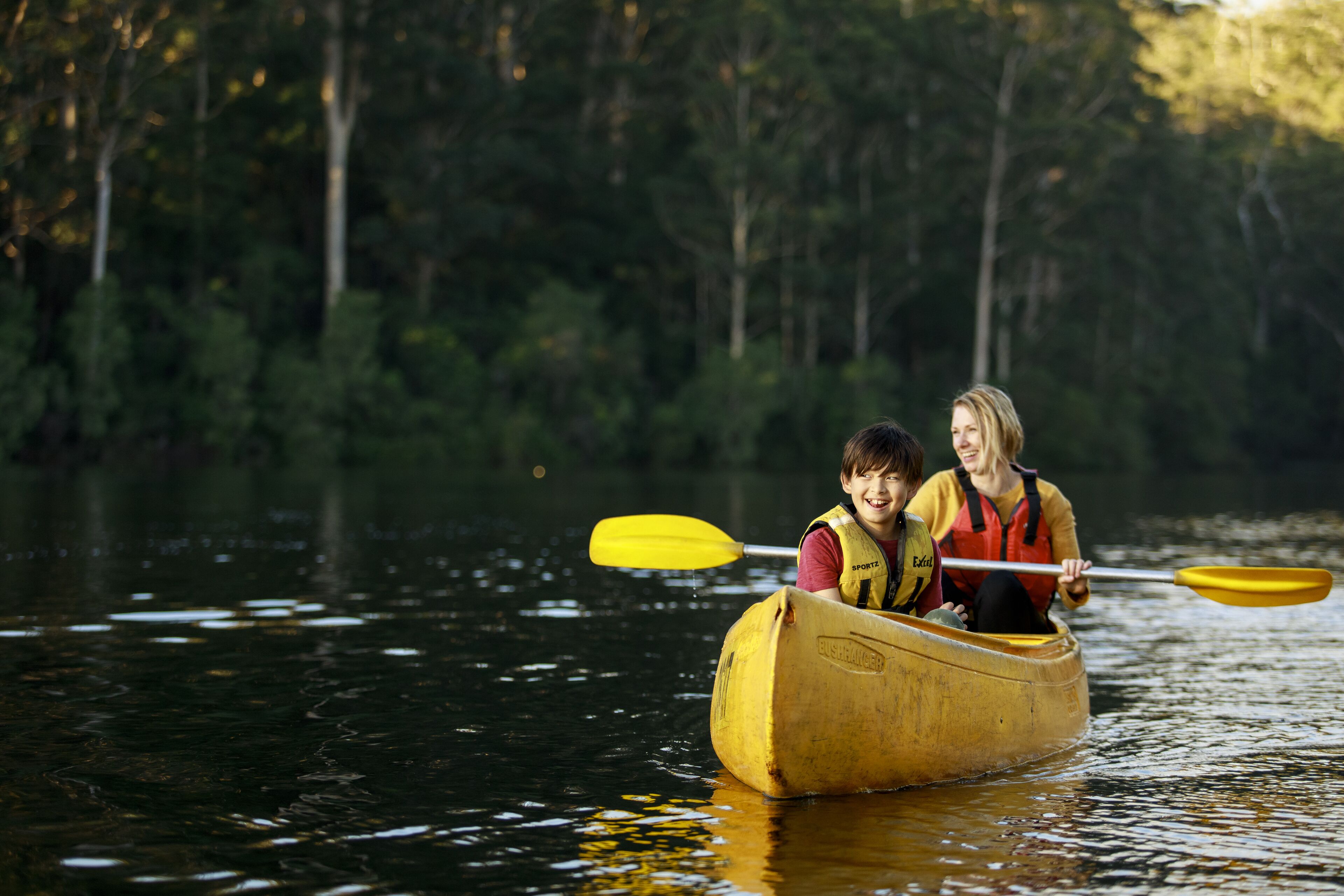 Two people in a canoe on a calm body of water surrounded by trees.