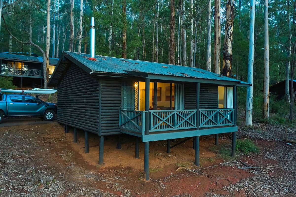 A wooden cabin with a balcony, surrounded by tall trees.