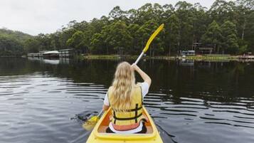 Une personne fait du kayak sur un lac calme, avec une rive boisée en arrière-plan.