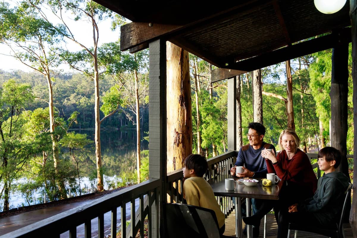 A covered outdoor seating area with a view of a forest and a body of water.