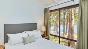 Une chambre à coucher avec un grand lit, deux lampes de chevet et une vue sur les arbres et l’eau, visible par une fenêtre.