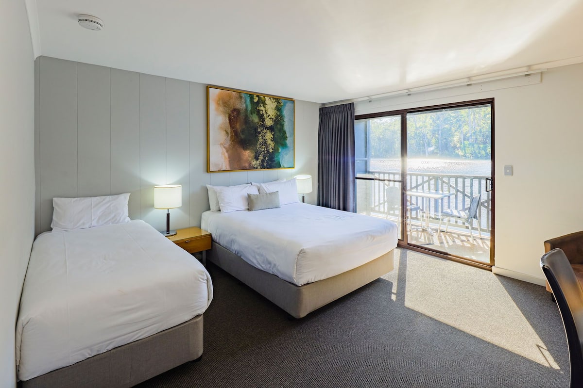 A hotel room with two beds, a large window, and a balcony.