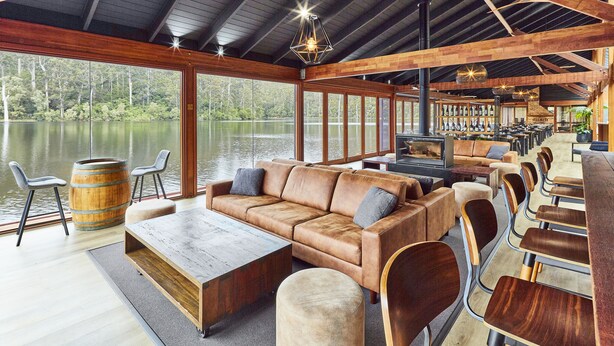 Un espace intérieur vaste et accueillant, avec une grande table en bois, un canapé en cuir et un coin bar donnant sur un lac.