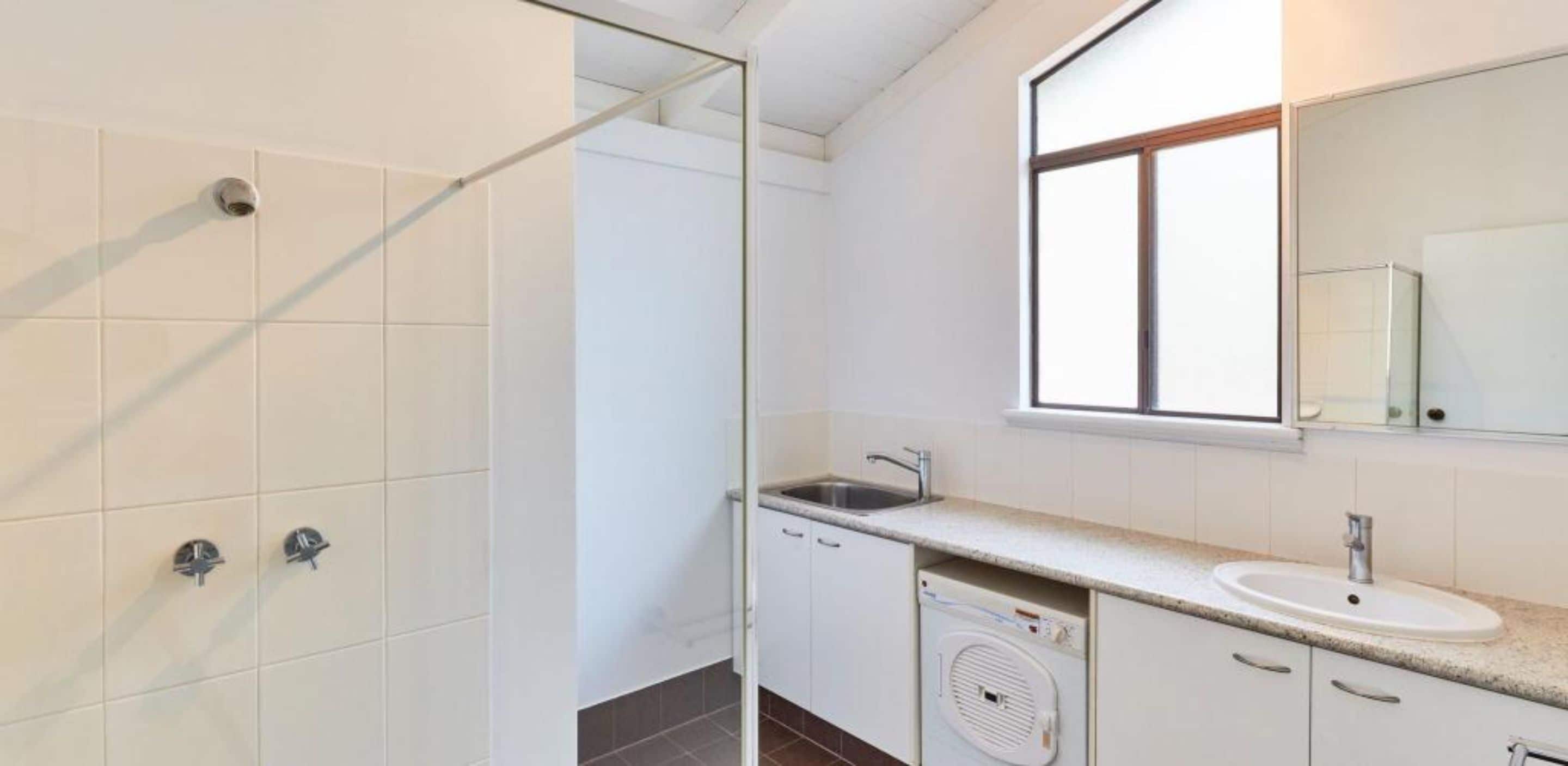 A modern bathroom with a glass shower enclosure, a sink with a mirror, and a built-in washing machine.