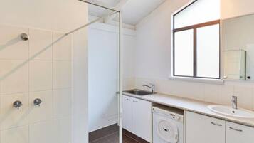 A modern bathroom with a glass shower enclosure, a sink with a mirror, and a built-in washing machine.