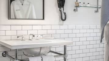 Une salle de bain avec un lavabo blanc, un miroir, un sèche-cheveux et une étagère en verre où sont rangés les articles de toilette.
