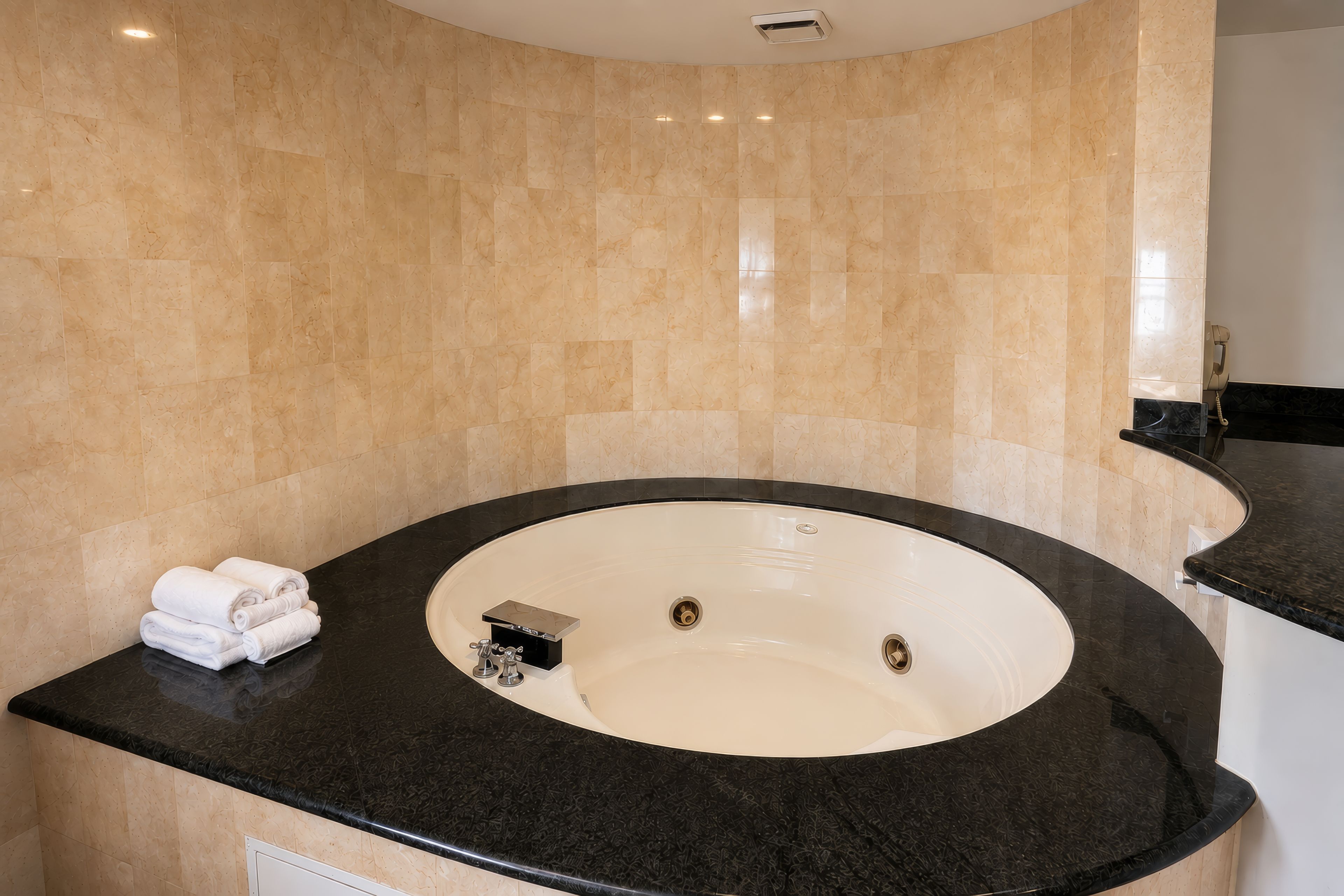 Un baño con una bañera grande, una encimera negra y una pared de baldosas color beige.