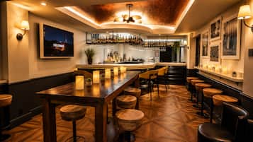 A bar area with wooden flooring, bar stools, a long bar counter, and a television displaying 'Hollywood'.
