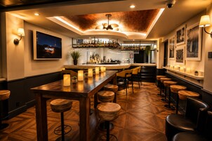 Angolo bar con pavimento in legno, sgabelli da bar, un lungo bancone e un televisore che mostra 'Hollywood'.