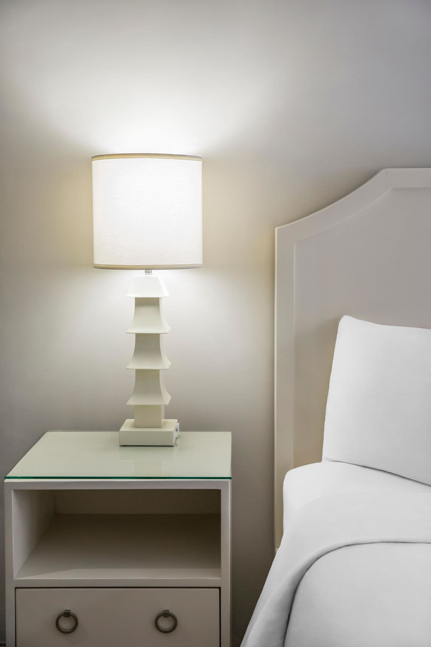 A modern bedside table with a lamp, a drawer, and a bed with a headboard.