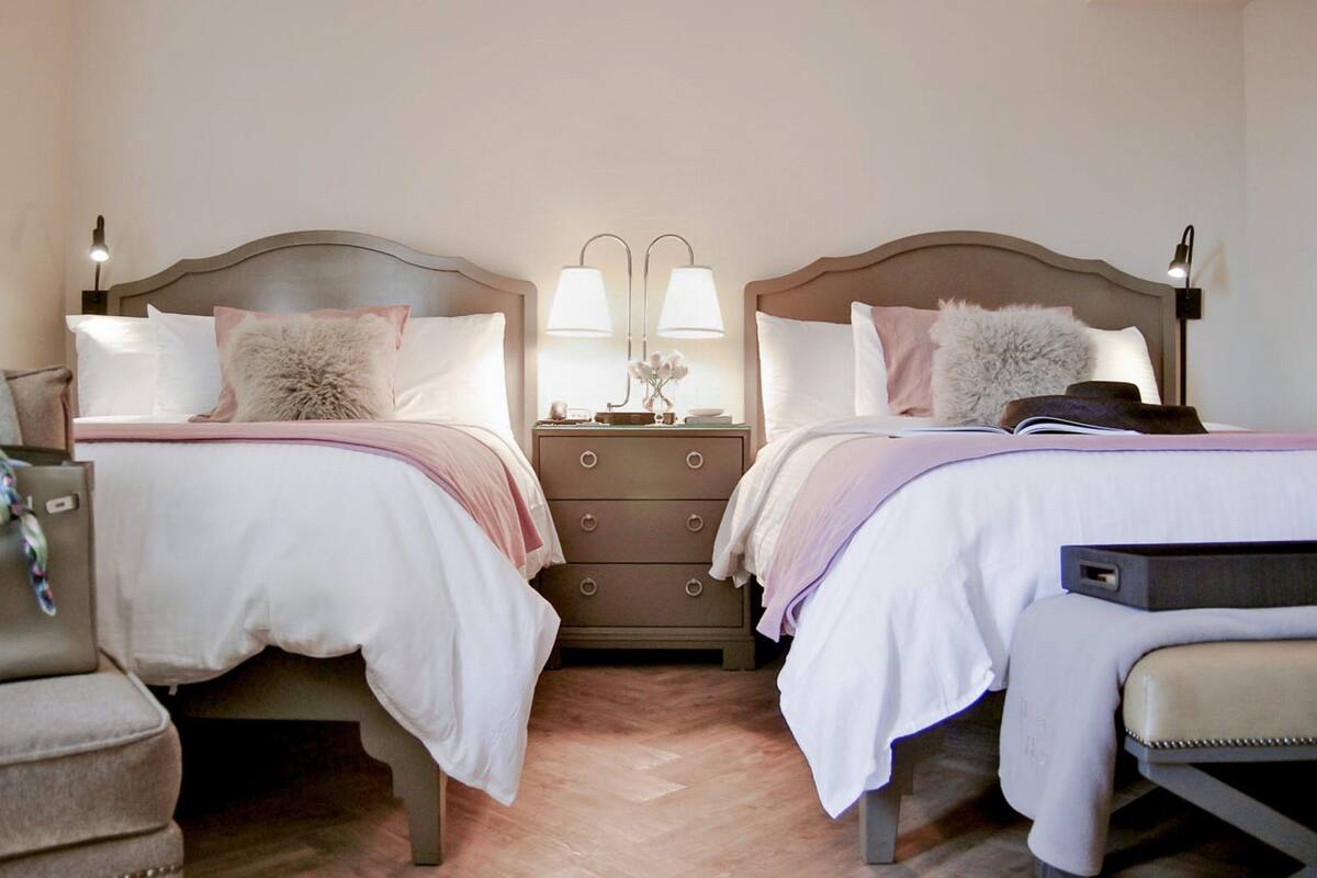 A hotel room with two beds, a dresser, and a chair.