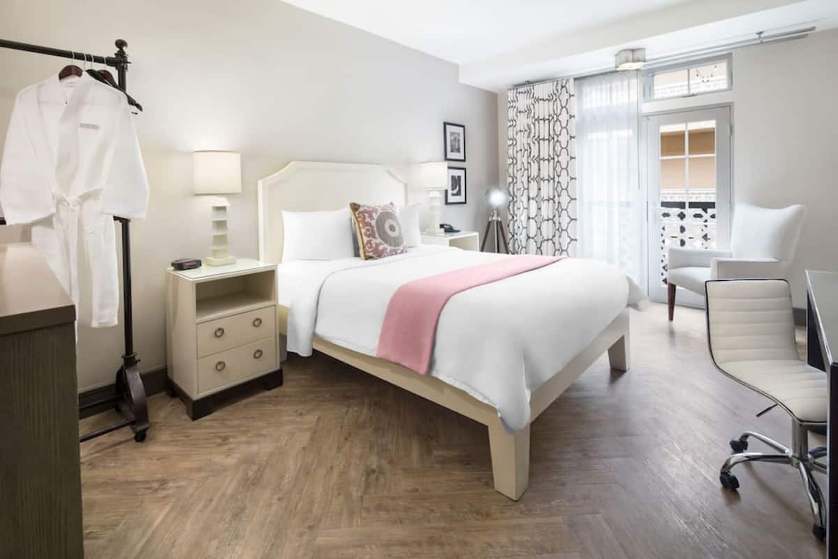 A hotel room with a bed, bedside table, lamp, chair, and a view of the balcony.