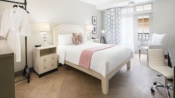 A hotel room with a bed, bedside table, lamp, chair, and a view of the outside through a window.