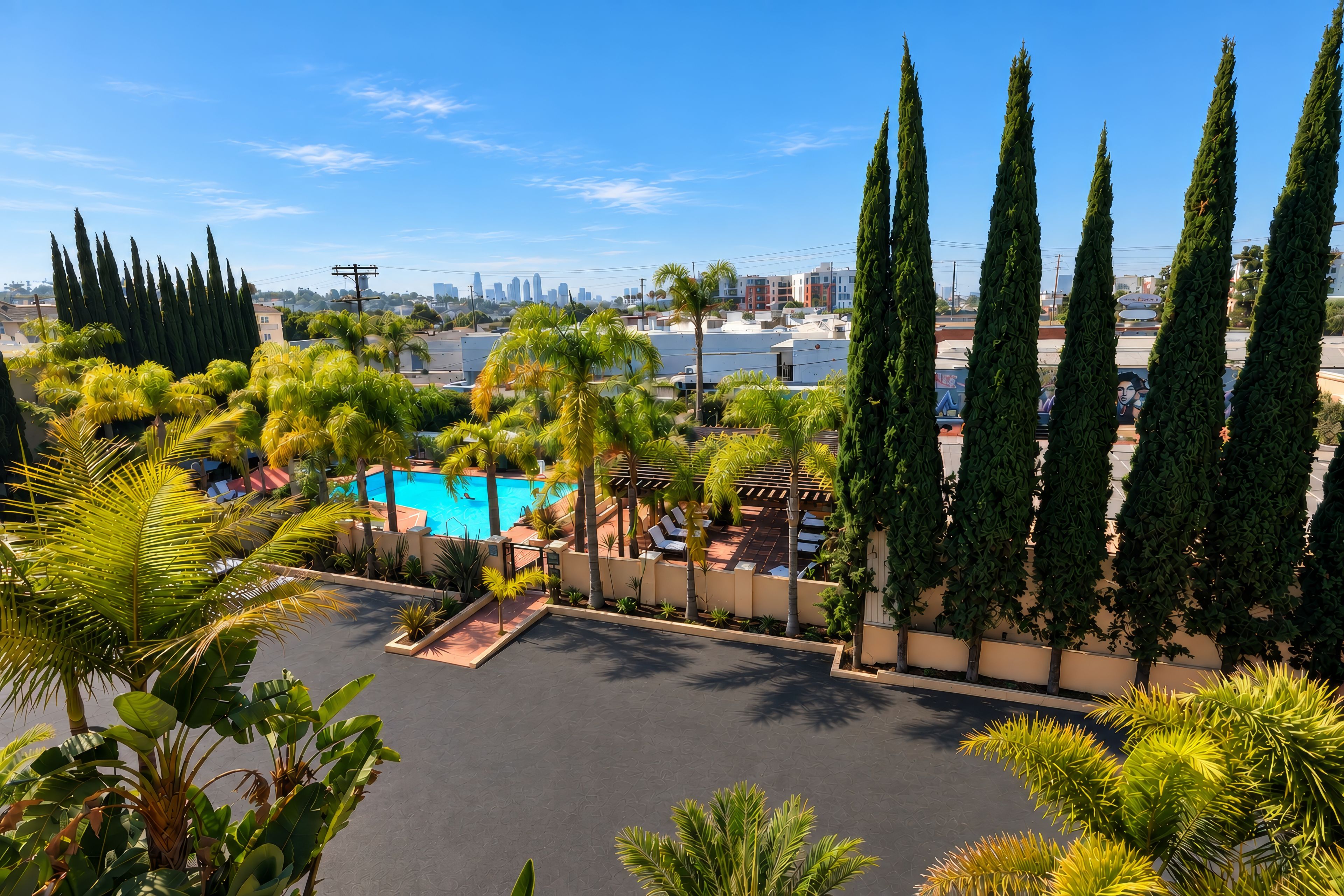 A pool area with palm trees, a clear sky, and a cityscape in the background.