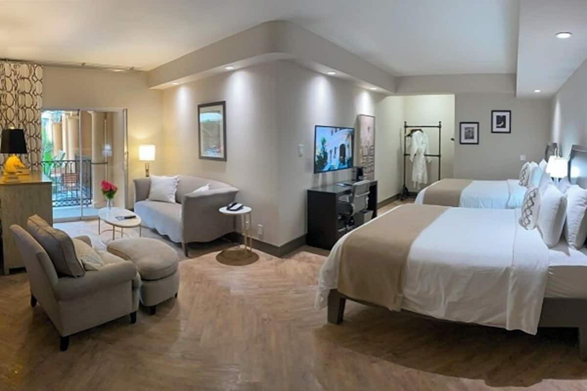 A modern hotel room with a sofa, two beds, a TV, and a desk.
