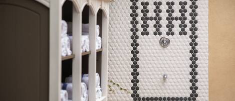 A bathroom with a tiled wall, a shower area, and a shelf with towels.