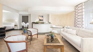 Um saguão de hotel com balcão de recepção, um sofá, duas poltronas, uma mesinha de centro e uma cama ao fundo.