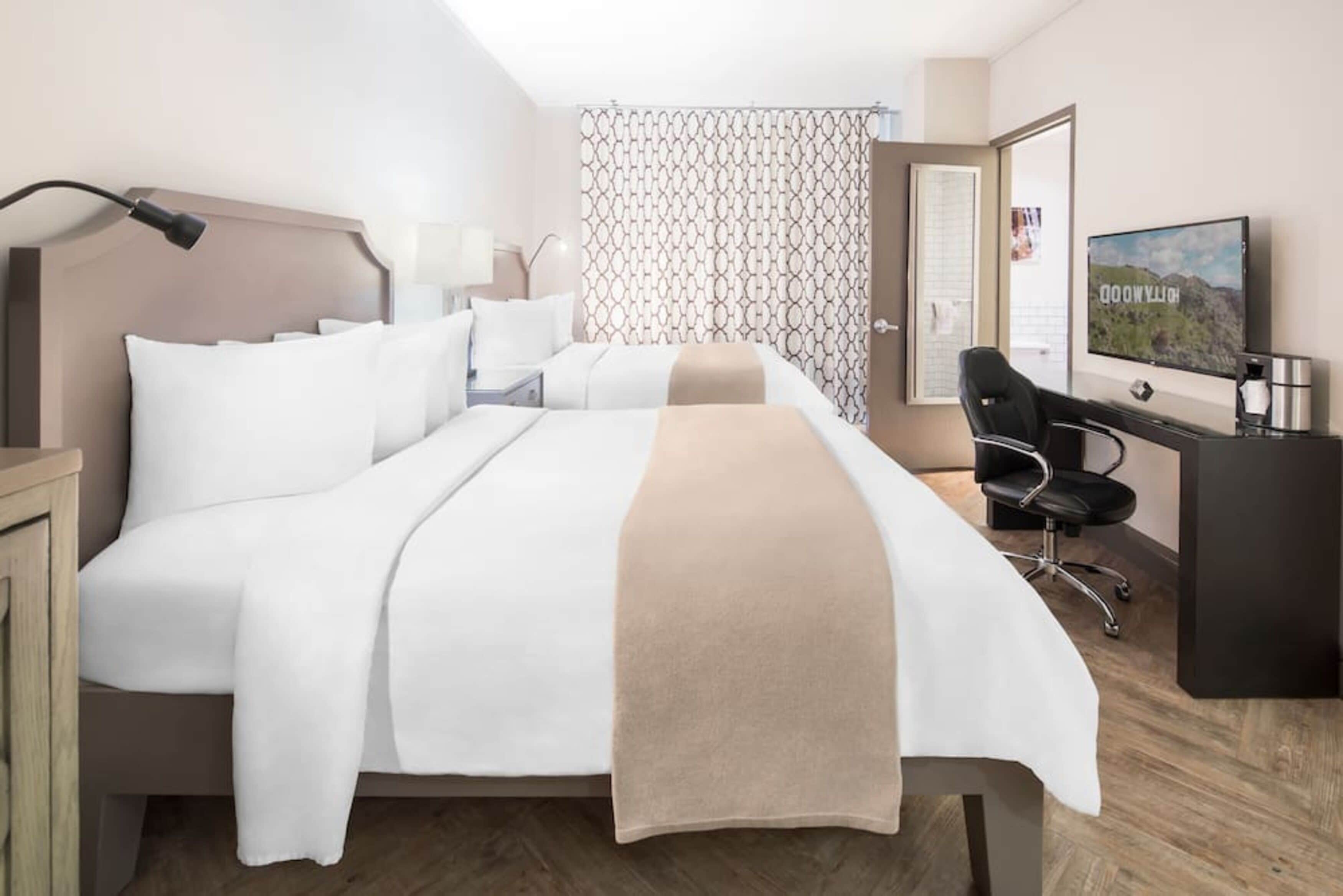 Habitación de hotel con cama, escritorio, silla, televisor y cortina estampada.